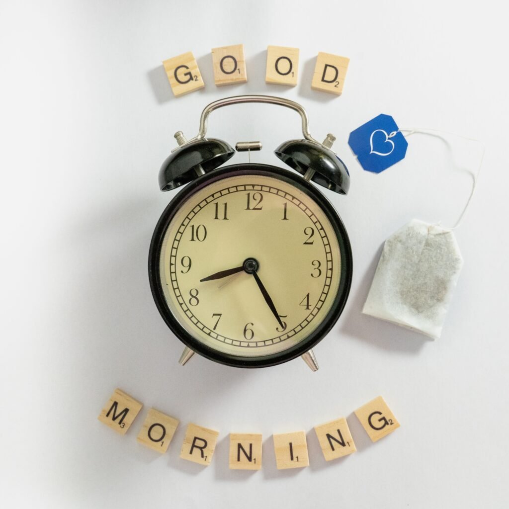 A charming flat lay of a vintage alarm clock with scrabble tiles spelling 'Good Morning' and a tea bag.