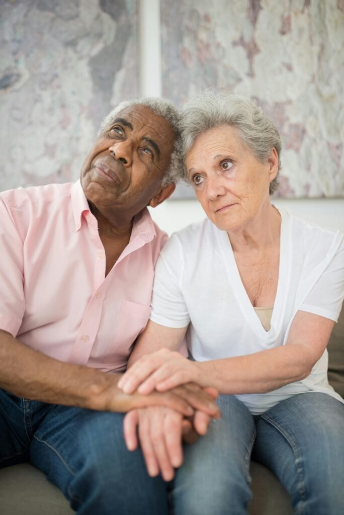 Elderly couple holding hands, expressing support and contemplation.